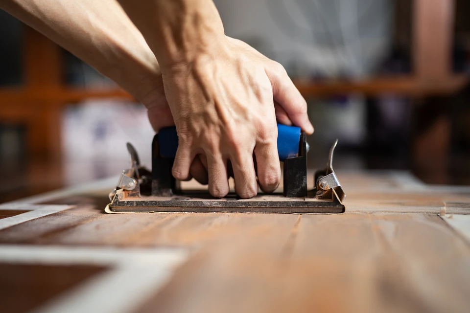 Artisan menuisier utilisant un rabot manuel sur planche de bois dans atelier traditionnel